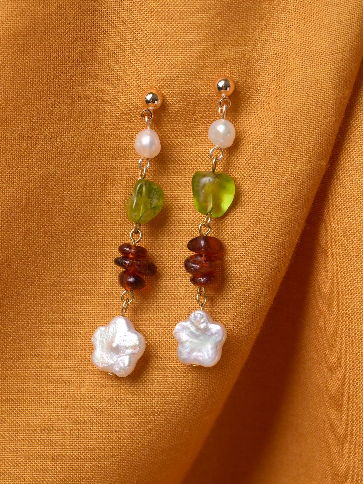 Closeup product shot of Studio Greco's handmade Persephone Earrings. These cascading drop earrings feature peridot and garnet gemstones as well as pearls. The earring stud is made with tarnish-resistant gold-plated brass.