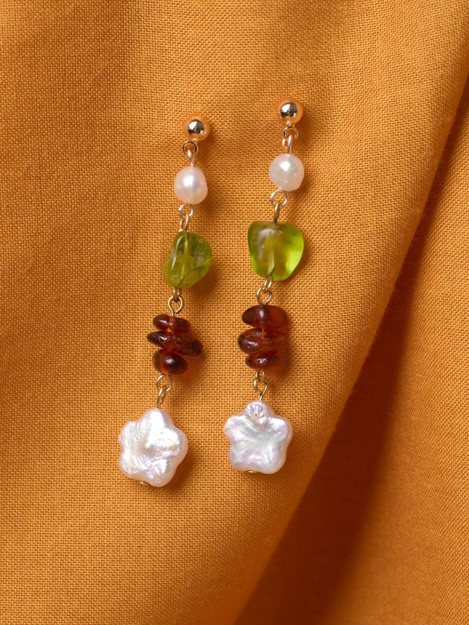 Closeup product shot of Studio Greco's handmade Persephone Earrings. These cascading drop earrings feature peridot and garnet gemstones as well as pearls. The earring stud is made with  tarnish-resistant gold-plated brass.